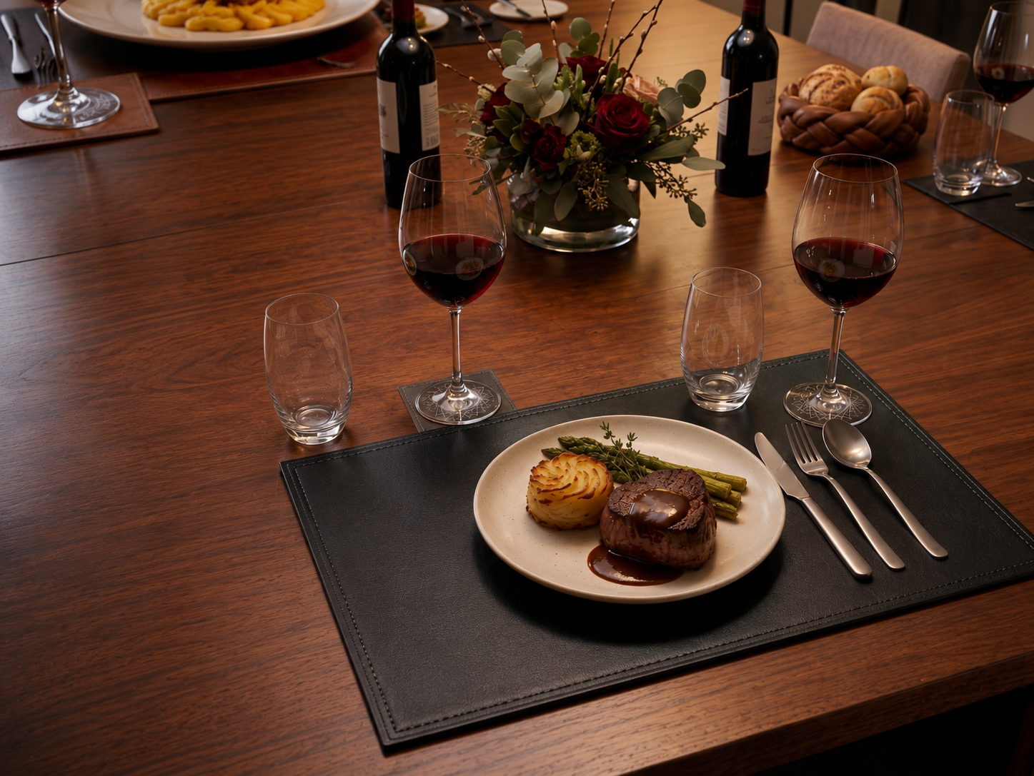Dinner table setting with a plate of food, wine glasses, and cutlery on a wooden table.