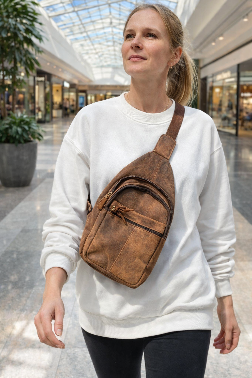 “Woman wearing brown leather sling chest bag in mall walkway”